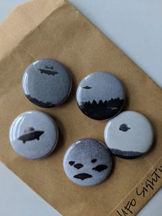 four buttons that have been placed on top of a piece of brown paper with black and white designs