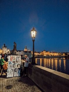 some people are standing by the water and looking at pictures on a street light pole