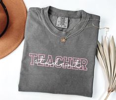 a t - shirt with the word teacher on it next to a hat and feathers