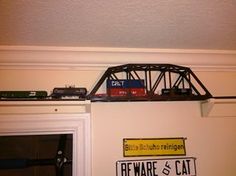 a toy train set on top of a shelf above a door with a sign that says beware and cat