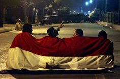 three people sitting on a bench with a large flag covering them from the sun at night