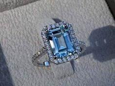 an aquamarine colored diamond ring sitting on top of a piece of cloth with diamonds around it