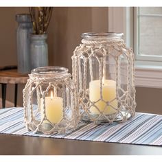 two glass jars with candles inside sitting on a table