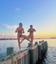 two women in bikinis are standing on a dock by the water and posing for a photo