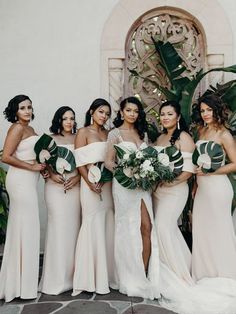 a group of women standing next to each other in front of a white building with greenery