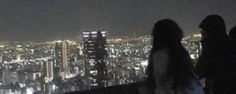 three people standing on top of a tall building at night with city lights in the background