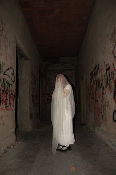 a woman in a white veil and black shoes walking down a dark hallway with graffiti on the walls