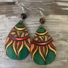 wooden earrings with colorful designs and beads hanging from them on a wooden surface, one earring has a bead in the middle