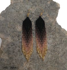 black and gold beaded fringe earrings sitting on top of a rock