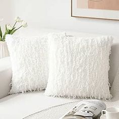 two white pillows sitting on top of a couch next to a vase filled with flowers