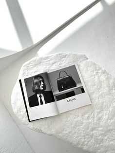 an open magazine with a woman's purse on top of the book is sitting on a rock