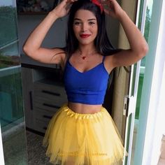 a woman in a blue top and yellow tulle skirt posing for the camera with her hands on her head