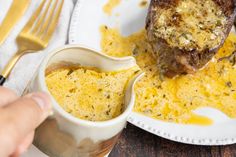 someone is dipping some food into a small bowl on a plate next to a fork and knife