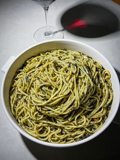 a white bowl filled with pasta next to a glass of wine