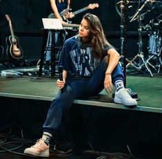 a man sitting on top of a stage next to a woman with guitar in the background