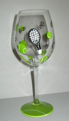 a wine glass with a tennis racket painted on the bottom and green trimmings