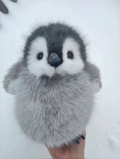 a hand holding a stuffed animal that looks like a penguin with fur on it's head