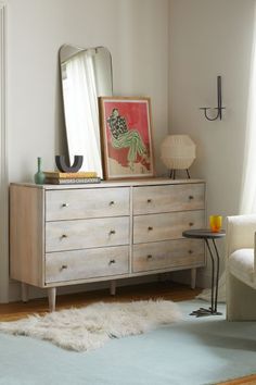 a bedroom with a dresser, mirror and lamp on it's side table in front of a window