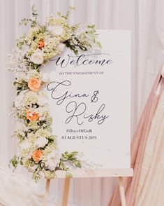 a welcome sign with flowers and greenery is displayed in front of a white curtain