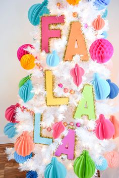 a white christmas tree decorated with colorful paper ornaments and the words fa la la on it