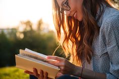 a woman is reading a book outside in the sun with her hair blowing back and eyes closed