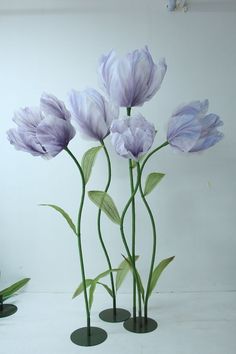 three vases with purple flowers in them on a white tableclothed surface, one has green stems and the other is made out of plastic