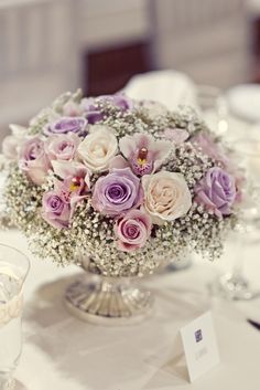 a vase filled with purple and white flowers on top of a table next to wine glasses