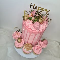 a pink birthday cake with cupcakes and decorations