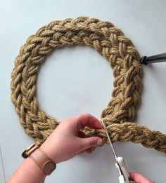 someone using scissors to crochet a rope around a wall hanging on the wall