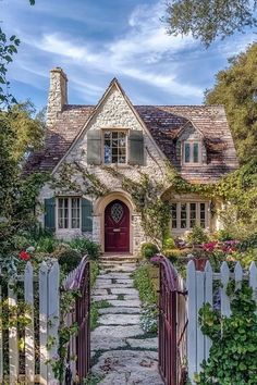 a white house with a red door surrounded by greenery and flowers in front of it