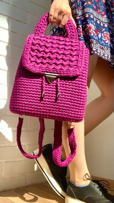 a woman carrying a pink crocheted purse on her feet, standing next to a white brick wall