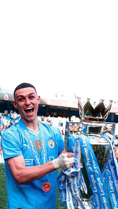 a man holding a trophy in his right hand and smiling at the camera while standing on top of a soccer field