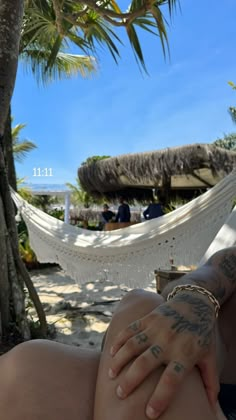 a woman laying in a hammock on the beach with her arm wrapped around her