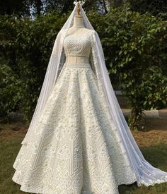 a white wedding gown with long sleeves and a veil on display in front of some bushes