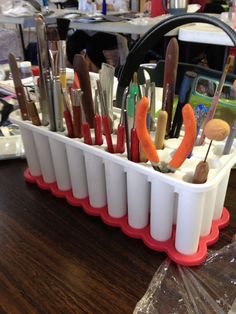 a container filled with lots of different types of paint brushes and spoons on top of a wooden table