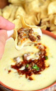 a hand holding a tortilla over a bowl filled with dip and toppings