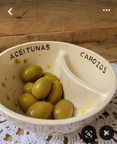 a white bowl filled with green olives on top of a doily covered table