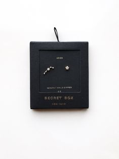 a pair of earrings in a black box on a white background with the words secret box written below it