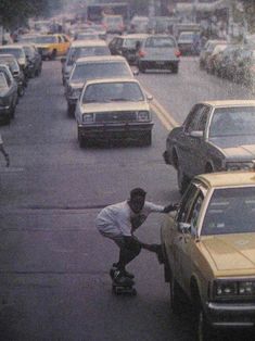 a man riding a skateboard down a street next to parked cars on a rainy day