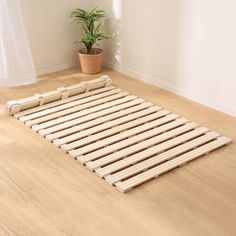 a wooden bed frame sitting on top of a hard wood floor next to a potted plant