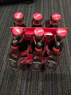 six bottles of coca cola sitting in a red crate on the floor next to a black bag