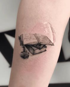 a black and white photo of a book tattoo on the left leg with an ink pen