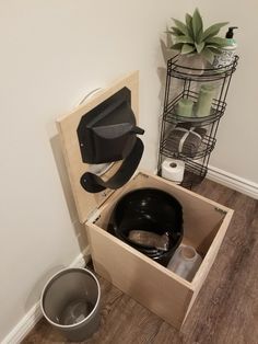 an open wooden box on the floor next to a trash can and toilet paper dispenser