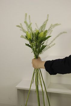 a person holding a vase with flowers in it on a white shelf next to a wall