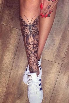 a woman's leg with tattoos on it and flowers in the bottom right corner