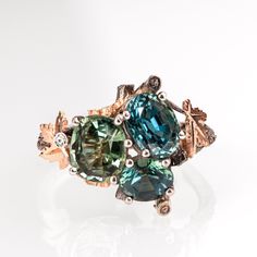 "An impressive ring made with 18k white gold, 14k rose gold, and platinum. Designed in a nature-inspired composition of twig and maple leaves set with a cluster of 3 exceptional sapphires. The sapphires are natural teal-green sapphires with a total weight of 5.48ct (1.78ct+2.53ct+1.17ct) The pictured ring is made in a size 8. This ring can also be made with different gold colors. You can also select one of the loose stones clusters from the images and this ring will be made with them - Cluster 1 - Moss agate cluster 1.52cttw Cluster 2 - Moss agate cluster 1.49cttw Cluster 3 - Blue sapphires 1.79cttw Cluster 4 - Moss agate cluster 1.69cttw Cluster 5 - Moss agate cluster 1.55cttw SOLD Cluster 6 - Tourmalines (1.03cttw) and triangle diamonds (0.15cttw) Cluster 7- Moissanites 2cttw Cluster 8 - Trendy Engagement Rings, Triangle Diamond, Purple Sapphire, Gold Colors, Loose Stones, Maple Leaves, Green Sapphire, Recycled Gold, Multi Stone Ring