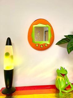 a frog sitting on the floor in front of a mirror and lamp next to a plant