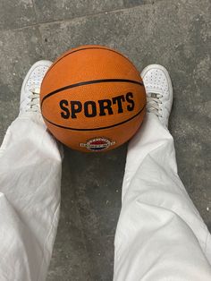 an orange basketball sitting on top of a person's white pants with their feet in the air