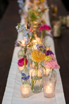 a long table with candles and flowers in vases on top of the tablescloth