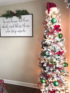 a white christmas tree with red, green and silver ornaments in front of a framed sign